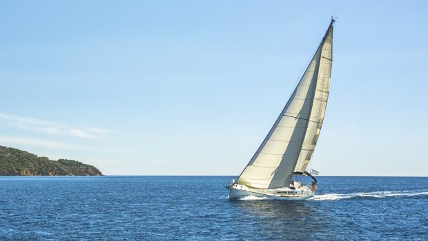 A sail boat on gliding by on calm ocean waters on a sunny day.