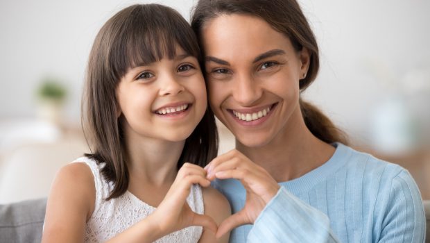 A young mother and daughter joining hands to create a heart shape.