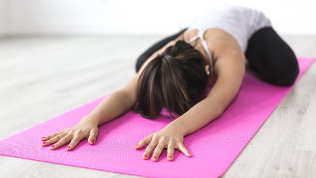 A woman doing a child pose on a pink yoga mat