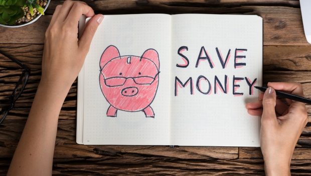 A pair of female hands drawing a picture of a piggy bank with the words "Save Money" next to it.