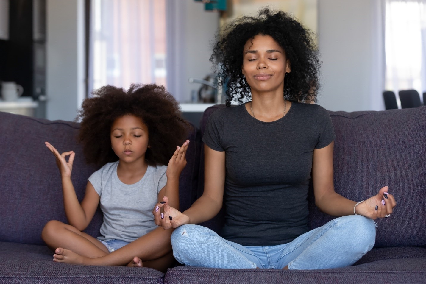 Mother and young daughter meditating on a couch