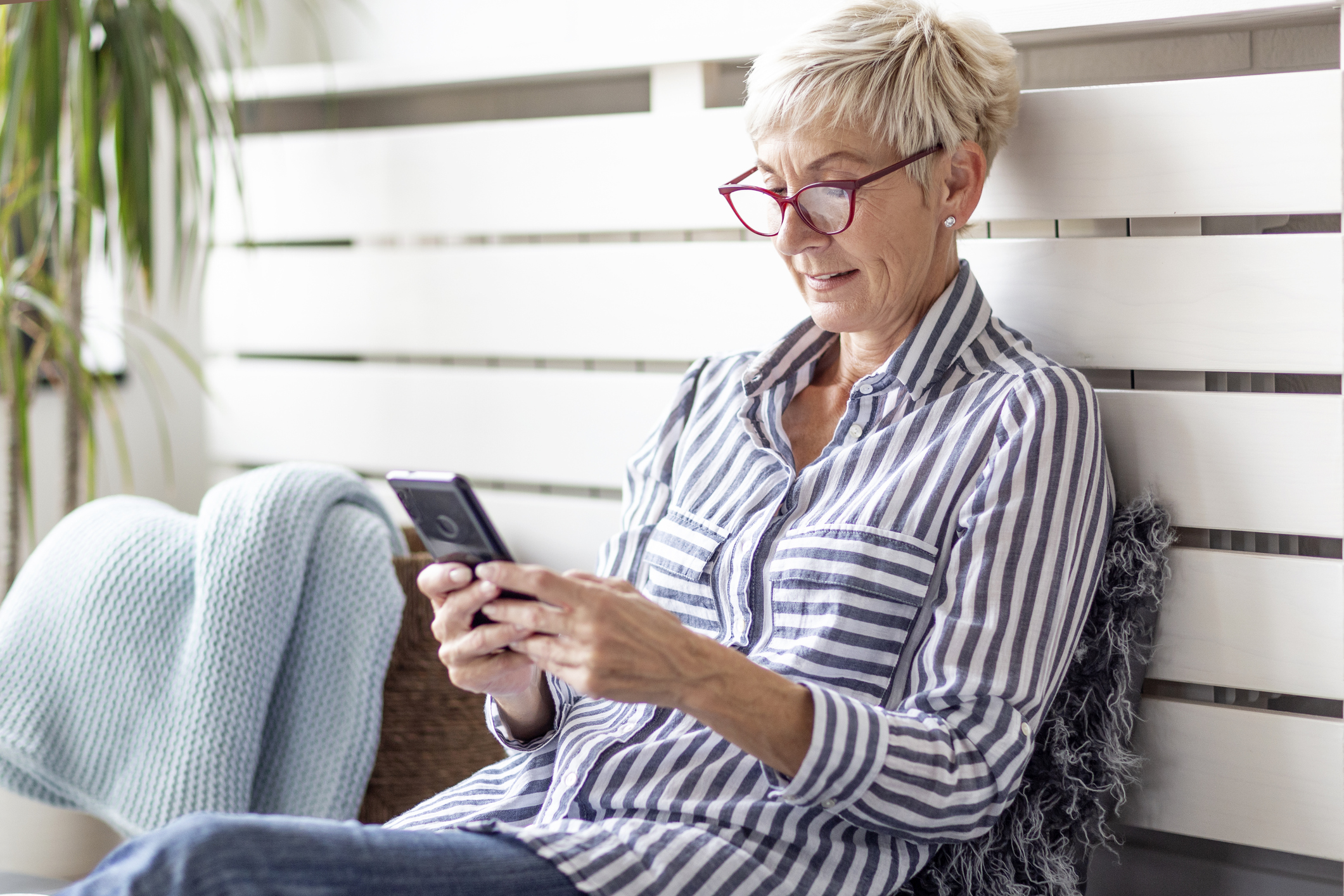 Mature woman with mobile phone on her hands sitting in room and sending messages to her friends and family