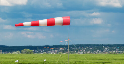 A red and white striped windsock blowing in the wind while planted in the middle of a green field