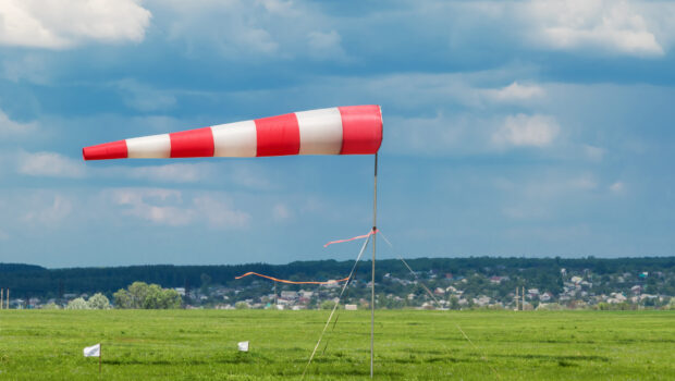 A red and white striped windsock blowing in the wind while planted in the middle of a green field